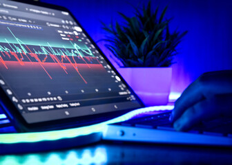Close-up of a person analyzing a volatile stock market chart on a tablet with neon lighting and modern workspace setup.