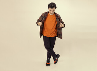 man wearing an orange shirt and checkered overshirt poses casually against a beige background