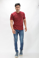 Young man wearing a red t-shirt, denim jeans, and sneakers posing casually in a studio against a...