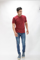 Young man wearing a red t-shirt, denim jeans, and sneakers posing casually in a studio against a...