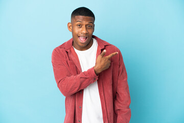 Young latin man isolated on blue background surprised and pointing side