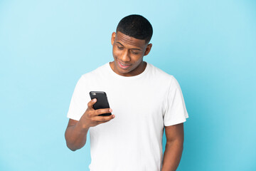 Young latin man isolated on blue background sending a message or email with the mobile