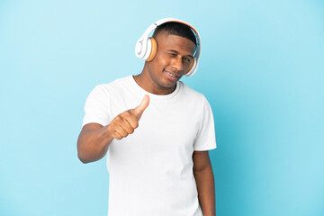 Naklejka premium Young latin man isolated on blue background listening music and with thumb up
