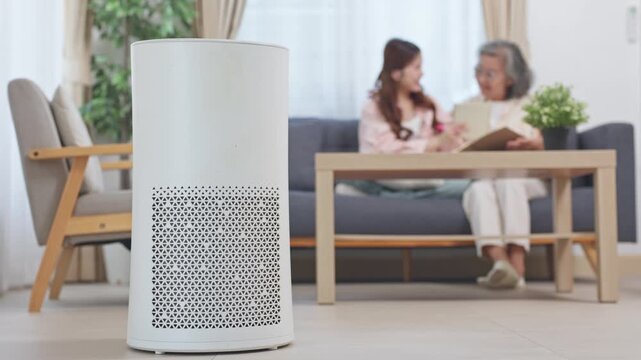 Air purifier in living room with wooden table and sofa, creating cozy home environment with natural light, peaceful clean indoor air for elderly and young women relaxing together