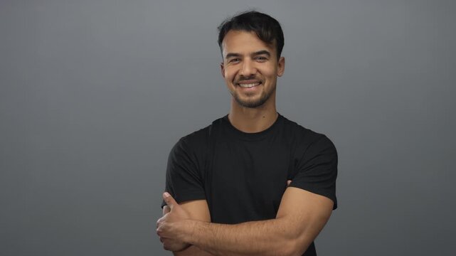 Young hispanic man smiling confidently against isolated grey background in casual black shirt showcasing friendly demeanor and positive attitude
