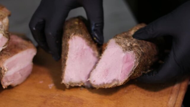 cut meat balyk hands in black latex gloves on a wooden board with a knife cut delicious meat slicing meat plate home cooking smoking