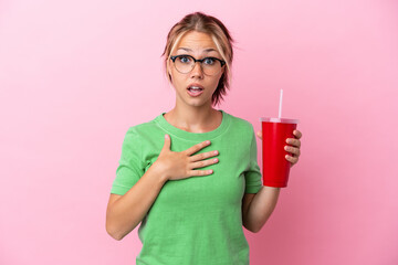 Young Russian woman holding a refreshment isolated on pink background surprised and shocked while...