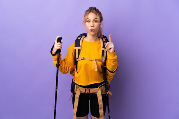 Teenager girl with backpack and trekking poles over isolated purple background intending to...