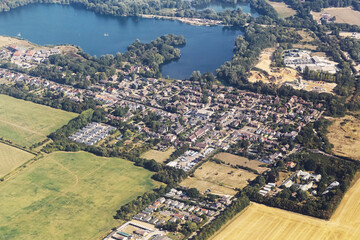 Aerial view of small town with lake. Houses and streets surrounded by green fields. Scenic countryside landscape with blue water and rural settlement. Summer day in natural environment from above.