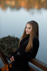 A woman stands on a wooden bridge near a picturesque pond. She leans on the railing.