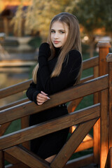A woman stands on a wooden bridge near a picturesque pond. She leans her hands on the railing.