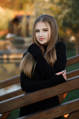 A woman stands on a wooden bridge near a picturesque pond. She leans her hands on the railing.