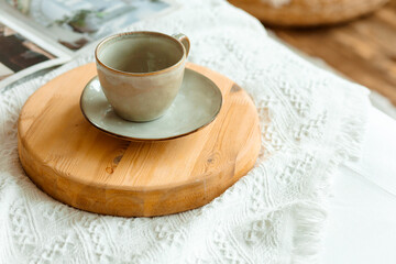 There is a ceramic coffee cup and saucer on a wooden stand. The atmosphere is cozy and warm, creating a feeling of morning calm.