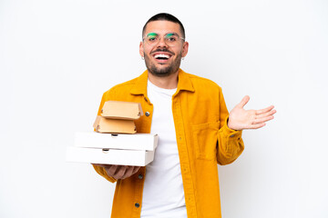 Young caucasian man holding pizzas and burgers isolated on background with shocked facial expression