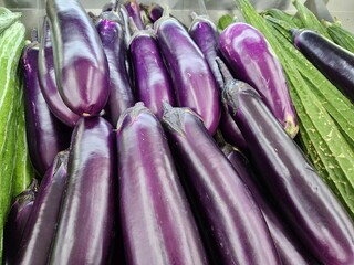 Abundant Fresh Purple Eggplants on Display Alongside Vegetables at a Market