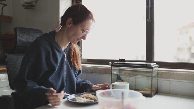 Woman eating breakfast in kitchen near fish tank