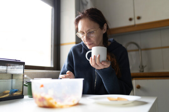 Woman drinking coffee and reading news on tablet at breakfast in kitchen