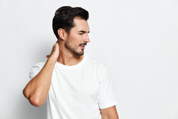 Confident young caucasian man wearing a casual white t-shirt touching his neck while looking away...