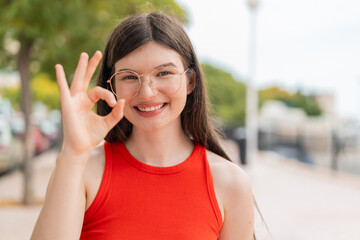 Fototapeta premium Young woman with glasses at outdoors showing ok sign with fingers
