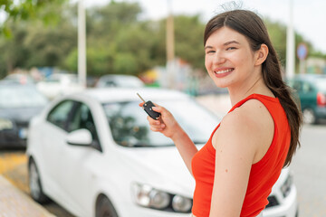Young pretty woman at outdoors holding car keys with happy expression