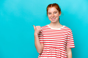 Young reddish woman isolated on blue background pointing to the side to present a product