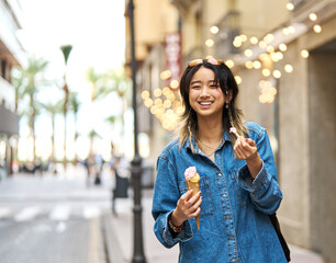 Portrait of a smiling young woman girl eating an ice cream walking in the city, tourists visiting...