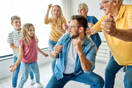 Portrait of a three generation famili, grandparents, parents and children playing and having fun dancing at home - Powered by Adobe