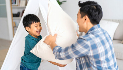 Fototapeta premium Happy Asian father and son enjoy a playful pillow fight in their living room, sharing laughter and creating joyful family memories together at home