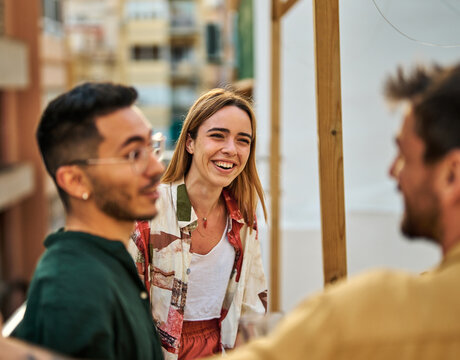 Happy young people having fun during a rooftop party during a summer holiday, standing on the rooftop terrace talking, eating and drinking, love, romance, relationship, flirting and youth culture conc