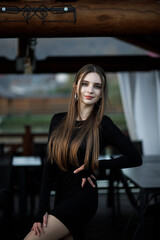A woman in a black dress with long sleeves stands on a wooden terrace