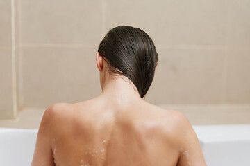 Relaxed woman bathing in a modern bathroom, her back turned while enjoying a moment of tranquility....