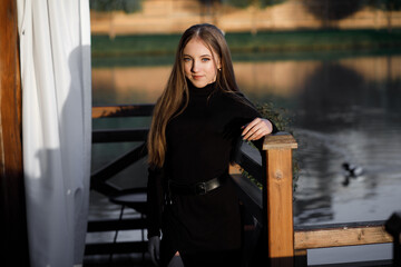 A woman stands on a wooden bridge near a picturesque pond. She leans on the railing.