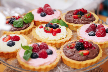 Assorted sweet tartlets with cream and berries. Delicious mini cakes with chocolate and fruit...