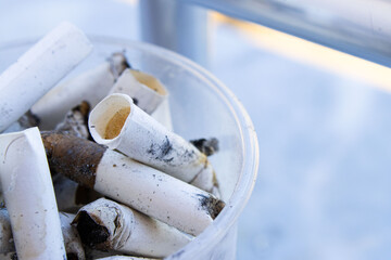 A cup overflowing with discarded cigarette butts on a marble bench