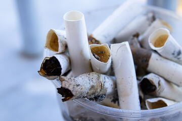 A cup overflowing with discarded cigarette butts on a marble bench