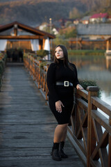 A woman stands on a wooden bridge near a picturesque pond.