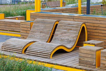 Two empty brown wooden deck chairs in the recreation area of the city park. The concept of summer holidays