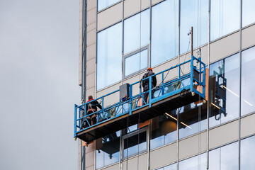 Two workers in a construction cradle are working at altitude. Installation work on the wall of a skyscraper