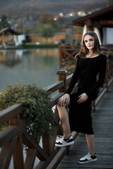 A woman on a wooden bridge. She has blond hair and a black dress with a slit.