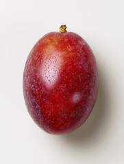 Close up view of a single red plum with water droplets on white surface