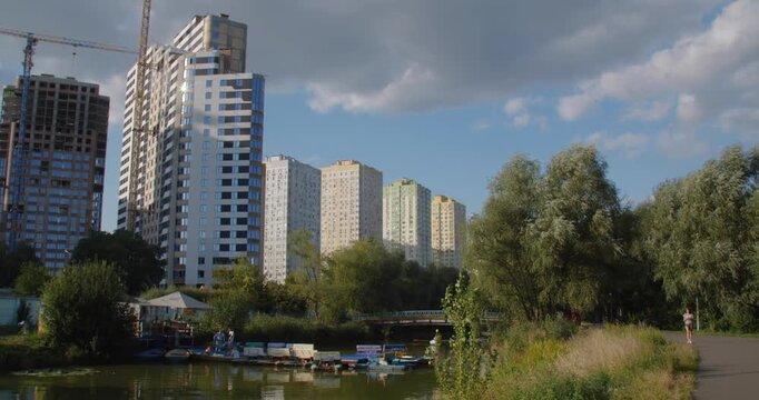 Lake in a beautiful city park on a sunny day. People rent boats and relax going for a row. New high-rise housing complexes are being built in the background.