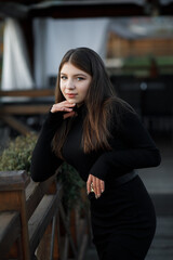A woman on a wooden bridge, she leans her hands on the handrails. She has blond hair and a black...