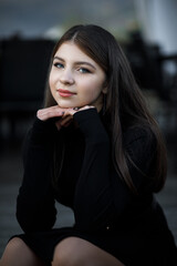 A woman in a black dress is sitting on the street, she holds her hands near her face