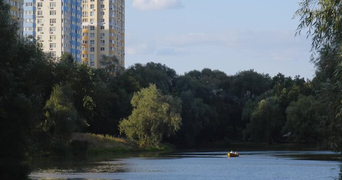 Lake in a beautiful city park on a sunny day. People rent boats and relax going for a row. New high-rise housing complexes are being built in the background.