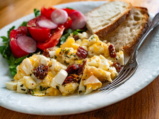 Scrambled eggs with feta cheese and dried tomato, bread and tomato salad on wooden table	