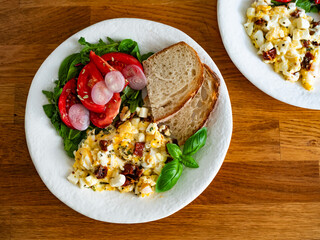 Scrambled eggs with feta cheese and dried tomato, bread and tomato salad on wooden table	