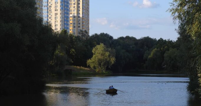 Lake in a beautiful city park on a sunny day. People rent boats and relax going for a row. New high-rise housing complexes are being built in the background.