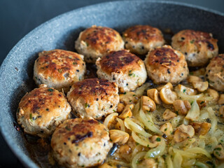 Frying pork meatballs with white mushrooms and onion in frying pan