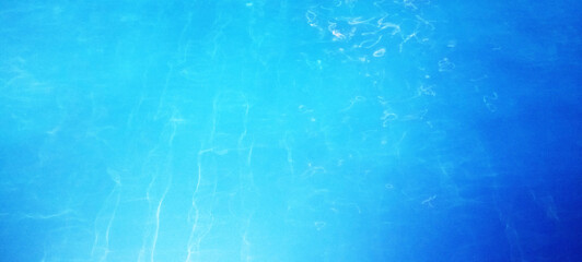 The crystal clear turquoise blue pool water surface gently ripples, reflecting sunlight and...