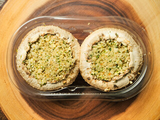 Two stuffed mushrooms in a plastic package on wooden background. Fine meal made of natural ingredients. Agriculture and farming, Food industry